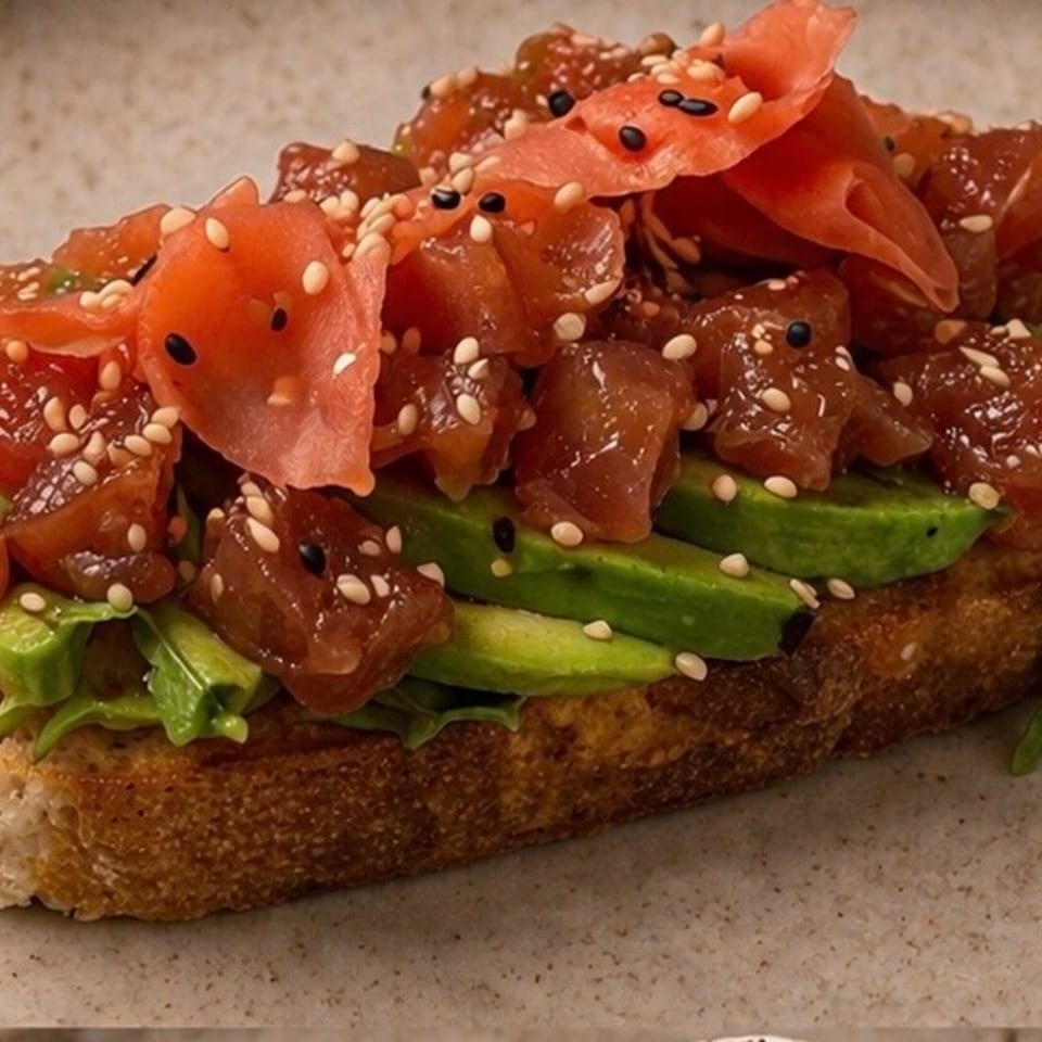 Tuna poke and avocado toast with sesame seeds and pickled ginger on a light plate.