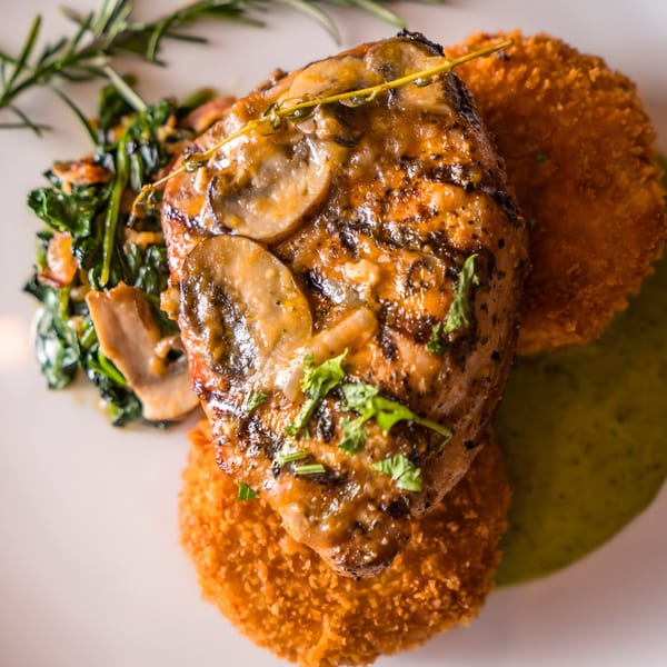 Mushroom-topped chicken breast with crispy potato cakes, sautéed spinach, and a sprig of rosemary.