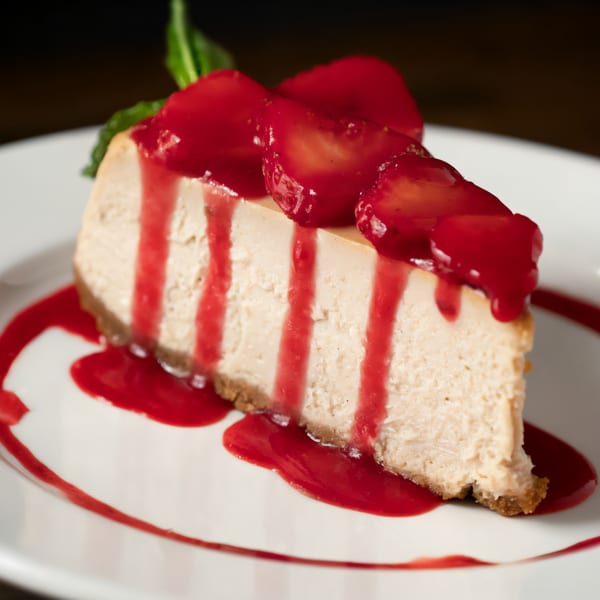 A slice of cheesecake with strawberry topping and sauce on a white plate.