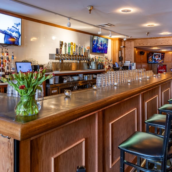 The Light Horse Restaurant and Bar's long wooden bar with stools, beer taps, liquor bottles, and TVs.