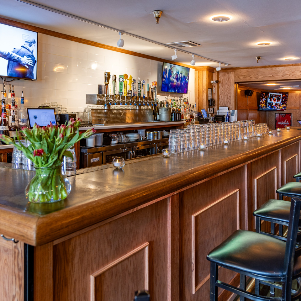 The Light Horse Restaurant and Bar's long wooden bar with stools, beer taps, liquor bottles, and TVs.