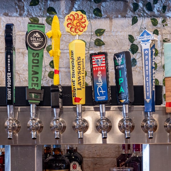 A row of six beer taps with various brewery handles, including Solace, Lawson's, Stone, and Port City.