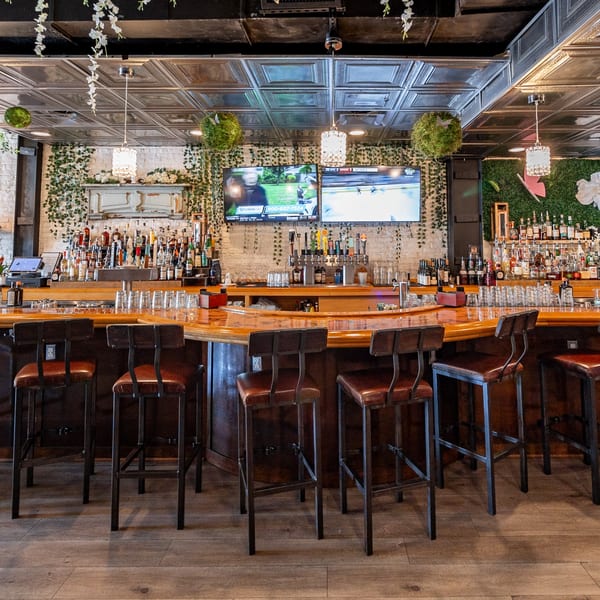 A long, curved wooden bar with stools, liquor bottles, beer taps, and TVs at The Light Horse.